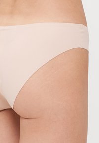Beżowe, bezszwowe figi bikini z niskim stanem, wykonane z miękkiego, elastycznego materiału, z gładkimi brzegami i minimalistycznym wzornictwem.