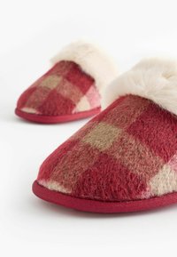 Punaiset ja beige ruudulliset tossut, jotka on valmistettu pehmeästä huovasta, ja niissä on pörröinen valkoinen tekoturkisl lining sekä punainen karhea pohja.