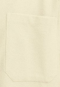 Crème-kleurige gebreide stof met een vierkant patch pocket met een gestructureerd oppervlak. De pocket heeft afgeronde hoeken en is netjes gestikt.