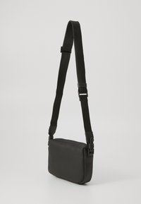 Geantă de umăr neagră, cu o textură netedă, formă rectangulară și curea ajustabilă. Dispune de accesorii mate și un design minimalistic.
