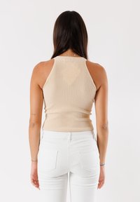 Canotta a coste beige con scollatura alta e design senza maniche, abbinata a pantaloni bianchi a vita alta con tasche posteriori.