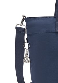 Borsa di tessuto blu navy con una superficie testurizzata, dotata di un ciondolo argento staccabile a forma di robot e di una tracolla resistente.