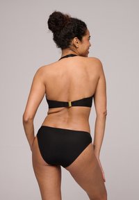 El conjunto de bikini negro con textura presenta un top halter con un broche dorado y una parte inferior de cintura alta.