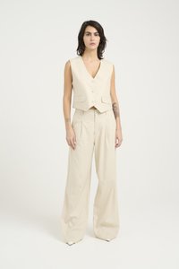 Beige mouwloze vest met een V-hals en knopen aan de voorkant, gecombineerd met wijde broekspijpen. Beide gemaakt van zachte, lichtgewicht stof.