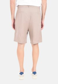 Pantaloni corti beige con una texture liscia, vita elastica e due tasche posteriori, abbinati a sneakers bianche con dettagli blu.