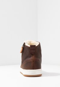Brown leather ankle boot with white sole, zip closure, fur lining, and tan accents. Textured material with minimal branding on heel.