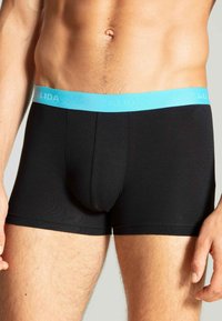 Zwarte boxershorts van gladde stof met een lichtblauwe tailleband waar de merknaam "CALIDA" in reliëf is gedrukt.