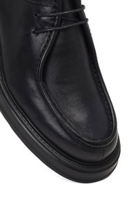 Stivale di pelle nera alla caviglia con punta rotonda, dettagli di cucitura in rilievo e chiusura con lacci. Presenta una suola in gomma testurizzata e una finitura liscia.