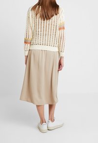 Pull crème en maille ouverte crochetée avec des accents multicolores, associé à une jupe midi beige fluide et des baskets blanches avec logo.