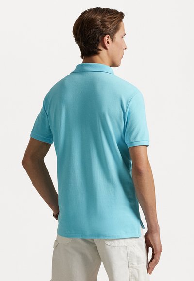 Polo de culoare albastru deschis, realizat dintr-un material texturat, având un guler clasic și mâneci scurte, cu slituri laterale la tiv pentru un plus de confort în mișcare.