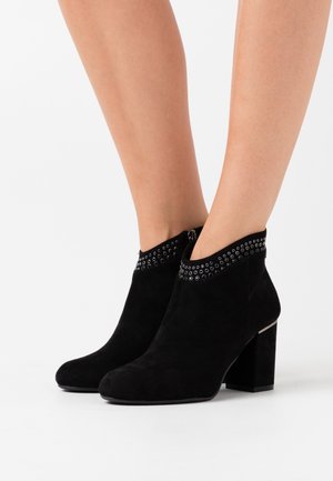 Bottines en suede noir avec un bout rond, un talon bloc et des accents cloutés autour du bord supérieur, dotées d'une fermeture à glissière sur le côté.