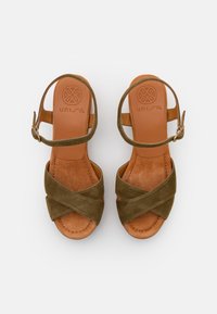 Sandales en daim vert olive avec des brides croisées, boucle de cheville réglable et semelle intérieure en cuir brun. Texture douce et design à bout rond.