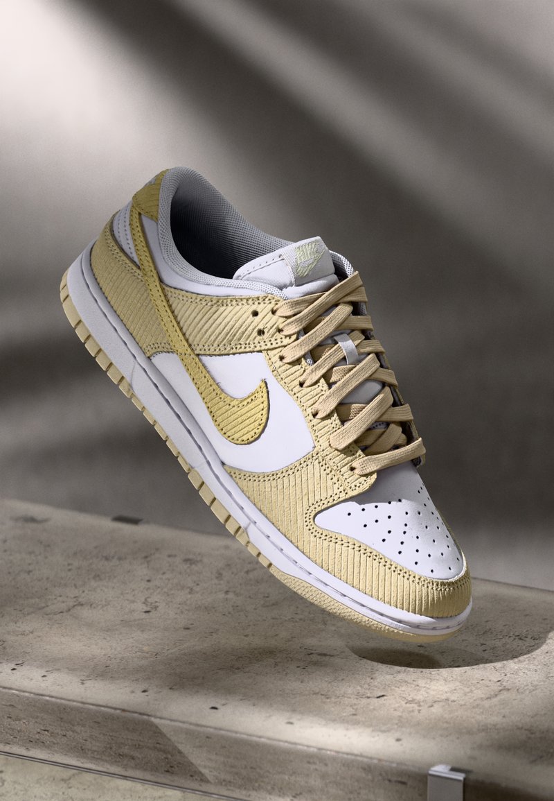Nike Dunk Low sneaker, amely fehér bőr és textúrált világos sárga panelek kombinációjával rendelkezik, szürke belső résszel és fűzőzárral.