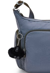 Borsa a spalla in tessuto grigio con molteplici tasche con zip, caratterizzata da un portachiavi a forma di gorilla nero peloso come dettaglio. Include una tracolla regolabile.