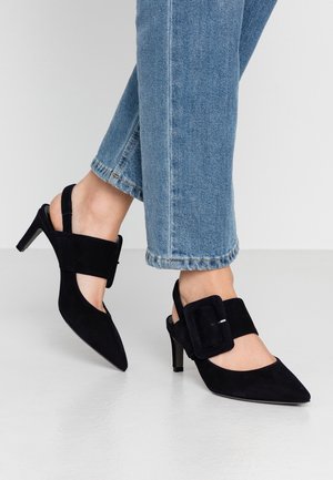 Czarne zamszowe szpilki z odkrytą piętą, zakończone spiczastym noskiem i średniej wysokości smukłym obcasem, z dużą prostokątną klamrą na pasku wokół kostki.