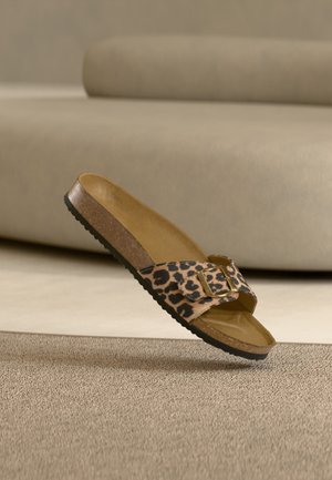 Σανδάλι τύπου slide με λωρίδα ζωηρού τύπου λεοπάρδαλης, χρυσή αγκράφα, πάτο από φελλό και μαύρη υφή σόλα πάνω σε μπεζ χαλί.