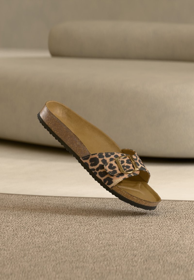 Σανδάλι τύπου slide με λωρίδα ζωηρού τύπου λεοπάρδαλης, χρυσή αγκράφα, πάτο από φελλό και μαύρη υφή σόλα πάνω σε μπεζ χαλί.