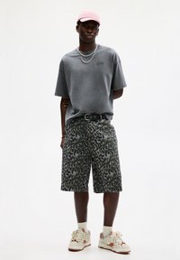 Grå oversized T-shirt, grøn leopardmønstret shorts, pink kasket, to sølvkæder, sort bælte. Hvide sneakers med orange accenter, beige sokker.