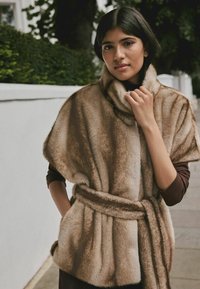 Brown faux fur poncho with a high collar, belted waist, and soft texture. Features wide sleeves and side pockets.