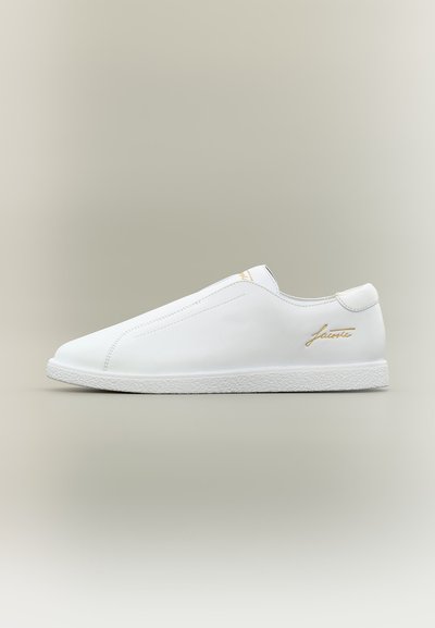 Бял спортен обувка тип слип-он с текстурирана подметка и златисто лого "Lacoste" отстрани, представена на неутрален фон.
