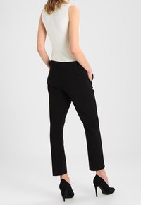 Pantalon noir fuselé avec une texture lisse, doté de poches latérales et d'une taille ajustée. Associé à un haut sans manches blanc à côtes et des talons noirs.
