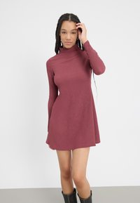 Bordo haljina dugih rukava s lažnim turtleneckom, rebrastom teksturom, prilagođenim gornjim dijelom i suknjom koja se širi, uparenim s crnim čizmama do koljena.