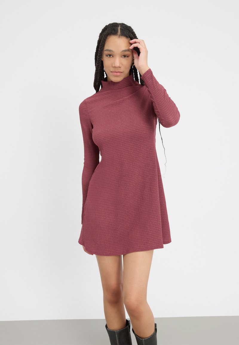 Bordo haljina dugih rukava s lažnim turtleneckom, rebrastom teksturom, prilagođenim gornjim dijelom i suknjom koja se širi, uparenim s crnim čizmama do koljena.