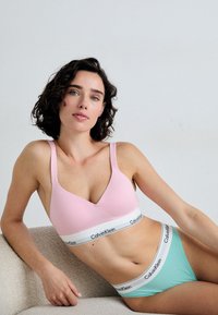 Světle růžový bralet s hlubokým V výstřihem a širokým šedobílým páskem Calvin Klein; máty zelené kalhotky se sladěným páskem. Hladká textilie.