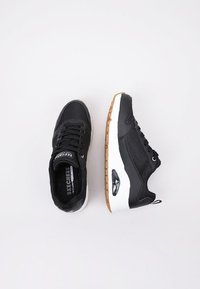Zapatillas deportivas negras con parte superior de malla texturizada, entresuela blanca y suela de goma natural. Cuenta con una unidad de aire visible y lengüeta con marca.