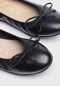 Bailarinas negras con un acabado de cuero suave. Cuentan con una punta redonda y un lazo en la parte frontal. Plantilla de espuma viscoelástica visible.
