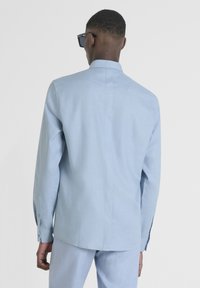 Camicia azzurra su misura a maniche lunghe con colletto strutturato, texture liscia e polsini abbottonati, vista dal retro.
