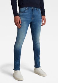 Skräddarsydda blå jeans med en gradienttvätt, med en femfickdesign och metallbeslag, bärs med vita sneakers.