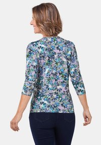 Bluse mit Blumenmuster und Dreiviertelärmeln, in Blau- und Grüntönen auf einem helllila Hintergrund. Glatte Stoffqualität, runder Ausschnitt.