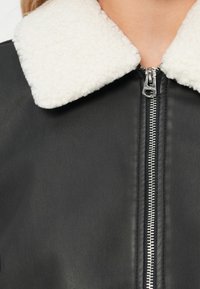 Μαύρο δερμάτινο μπουφάν με λευκό χνουδωτό γιακά και ασημένιο κλείσιμο φερμουάρ, αναδεικνύοντας τη λείος υφή και τα αντίθετα χρώματα.