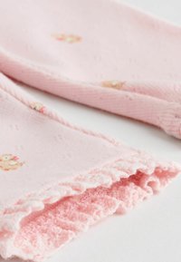 Rosa stickad tyg med en subtil textur, prydd med små djurmönster. Kanten har en volangkant som tillför en känslig detalj.