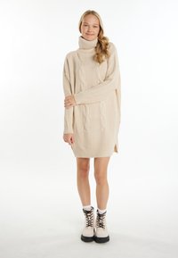 Rochie bej tricotată cu guler înalt, model cu motive de torsadă, slituri laterale și tiv din tricot. Modelul a asortat-o cu cizme crem cu șireturi și șosete albe.