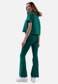 Zielony krótki top i rozszerzane spodnie z miękkiego materiału, w połączeniu z białymi tenisówkami. Strój charakteryzuje się luźnym krojem i gładką fakturą.