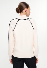 Suéter rosa claro con acentos negros, puños y dobladillo acanalados, con un cuello alto y mangas raglán, hecho de un material de punto suave.