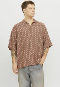 Camisa de manga corta, con botones, en marrón con un patrón geométrico en blanco. Hecha de un tejido ligero, presenta un corte relajado y cuello.