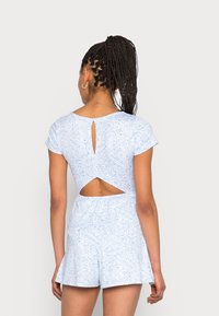 Macacão azul claro com padrão paisley, mangas curtas e recorte nas costas. Cintura elástica e calças curtas amplas, feito de tecido macio.