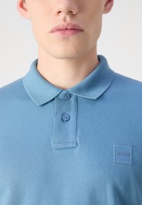 Blaues Poloshirt aus strukturiertem Material. Verfügt über einen klassischen Kragen, zwei Knöpfe und ein BOSS-Logopatch auf der linken Brust.