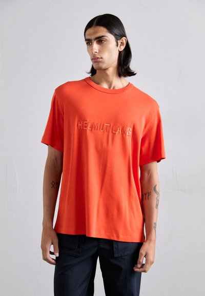 T-shirt en coton orange avec un col rond et des manches courtes. Présente un texte en relief "HELMUT LANG" sur le devant. Texture lisse.