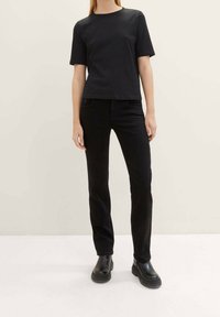 Camiseta de algodón negra de manga corta, combinada con jeans negros. El conjunto se complementa con botas negras de tobillo con suela gruesa.