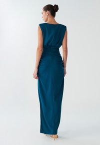 Sinine-rohelise tooniga põrandapikkune kleit, varrukateta disainiga, vöökoha kokkupõmmitud ning siledapinna tekstuuriga. Tagaküljel on peidetud luku sulgemine.