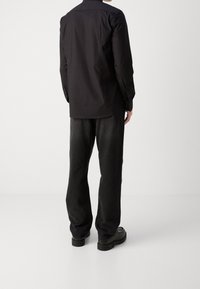 Camisa negra de manga larga, mezcla de algodón, con puños abotonados. Combinada con pantalones vaqueros oscuros y sucios y zapatos de cuero negros. Diseño limpio y minimalista.