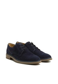 Chaussures en suede bleu marine avec un design classique à lacets, une semelle en caoutchouc marron clair et des accents de couture contrastants. Texture lisse.