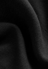 Tela negra con una textura suave y lisa, que muestra patrones de punto fino y un brillo sutil, cayendo en suaves pliegues.