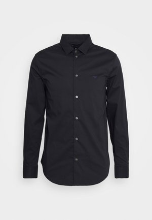 Camisa preta de manga longa com botões, feita de tecido suave, apresentando um colarinho clássico, mangas de comprimento completo e um pequeno logótipo no peito.