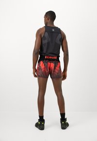 Schwarzes Sporttanktop mit Mesh-Elementen; rote und schwarze Shorts mit grafischem Design; schwarz-grüne Schuhe mit Logo-Detail.
