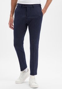 Granatowe spodnie w paski o dopasowanym kroju, z płaskim przodem, szlufkami na pasek i gładką fakturą, zestawione z białymi trampkami.